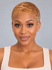 A woman with a short, textured blonde pixie cut wearing a cream ribbed tank top, photographed against a solid gray studio background.