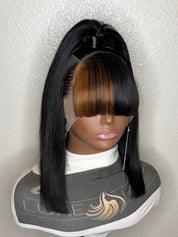 A black straight wig with a high ponytail and bangs displayed on a mannequin head against a textured off-white wall.