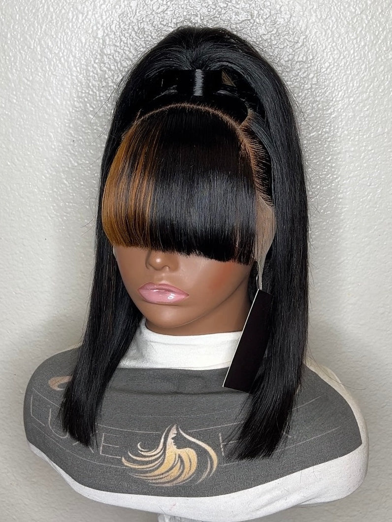 A black straight wig with a center part and bangs displayed on a mannequin head, set against a textured off-white wall.