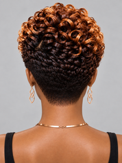 Back view of a woman with a short, styled afro hairstyle featuring dark brown to copper-blonde highlights, wearing gold hoop earrings and a gold chain necklace against a solid gray background.