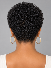 Back view of a person with short, tightly curled black hair, wearing large gold hoop earrings and a white ribbed top against a plain gray background.