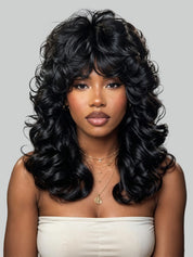 A woman with long, voluminous, black curly hair wearing a strapless cream top, photographed against a solid light gray background.