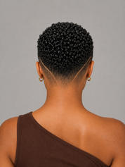 Back view of a person with a short, tightly curled black hairstyle and a side-swept fade, wearing small gold hoop earrings and a brown one-shoulder top against a plain gray background.