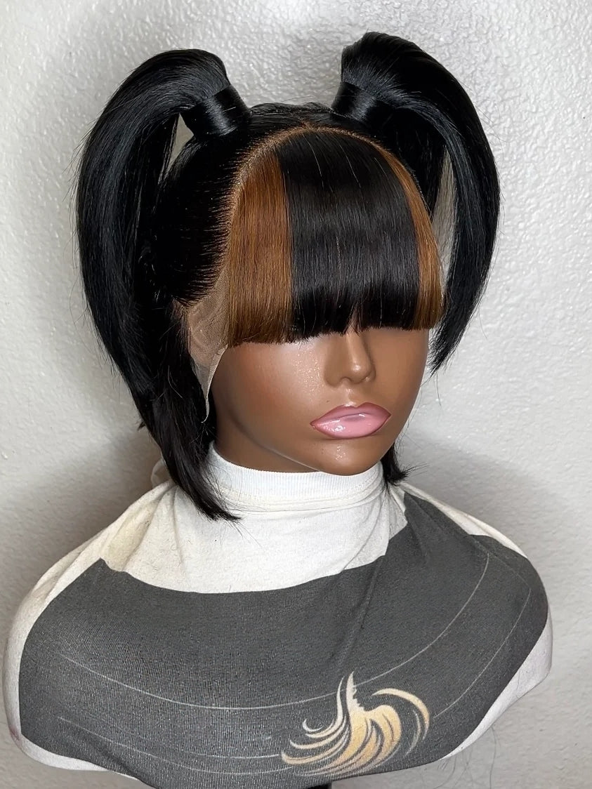 A black wig with two high pigtails and straight bangs, styled on a mannequin head against a light textured wall.