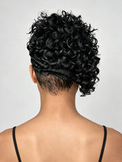 Back view of a person with short, curly black hair styled in a low bun with a side braid, wearing a black spaghetti strap top against a light gray background.