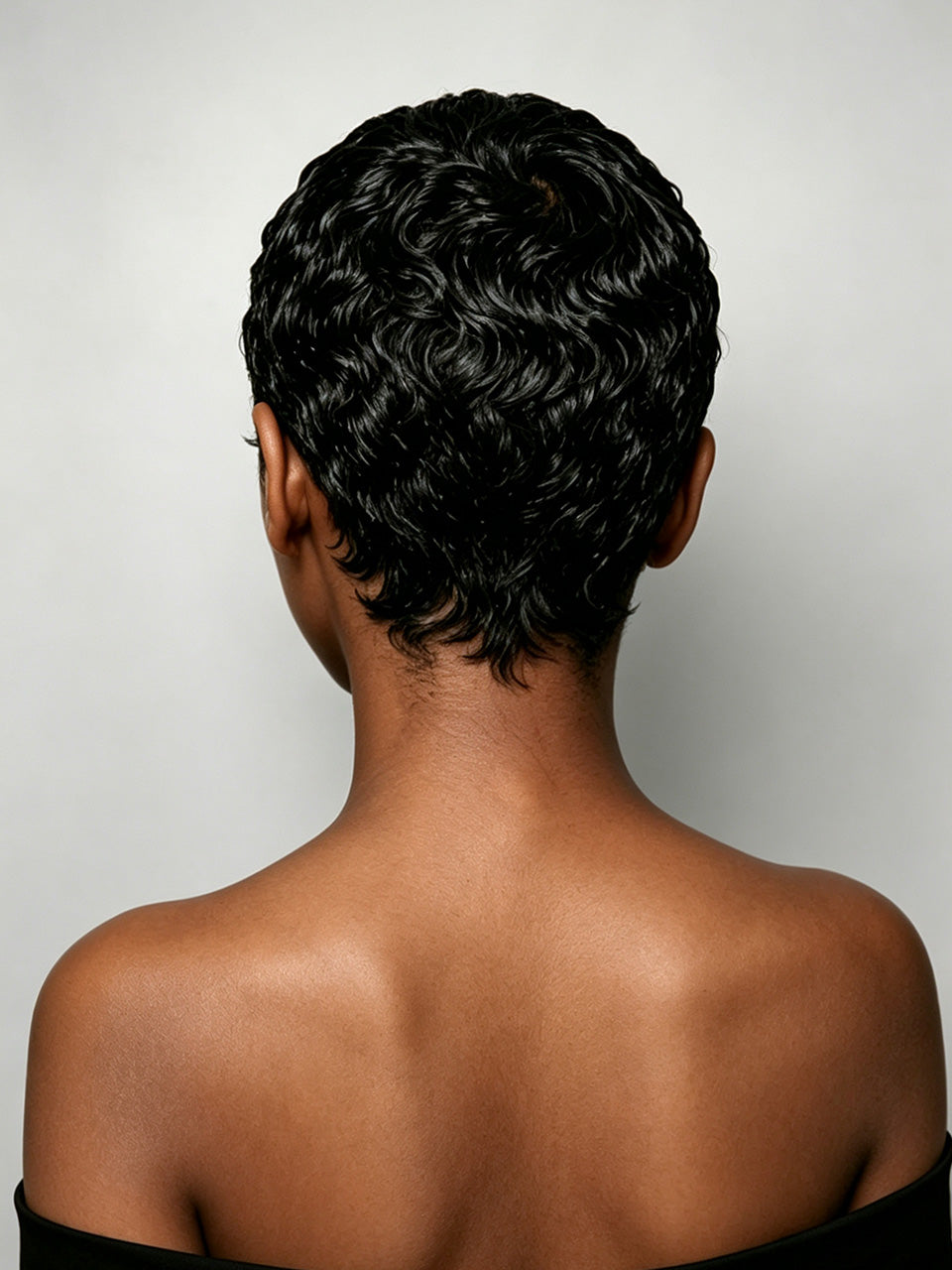 Back view of a person with a short, curly black wig against a light gray studio background.