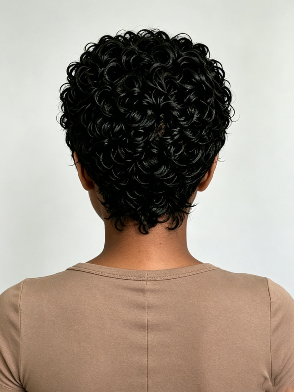 Back view of a person with short, tightly curled black hair wearing a beige crew-neck top against a light gray background.