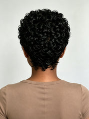 Back view of a person with short, tightly curled black hair wearing a beige crew-neck top against a light gray background.