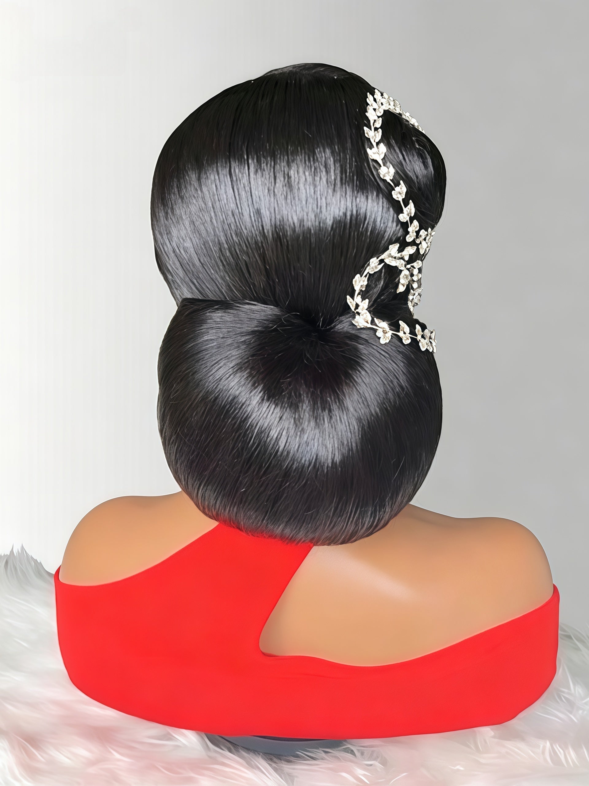 A mannequin bust with a large, glossy black updo hairstyle and a silver floral hair accessory, wearing a bright red top against a light gray background.