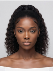 A close-up portrait of a model with a dark brown to black curly wig styled in a half-updo, wearing a white off-the-shoulder top against a light gray background.