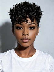 A close-up portrait of a person with a short, curly black wig or hairpiece against a light gray background, wearing a plain white crew-neck T-shirt.