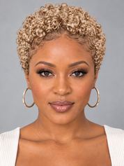 A woman with short, tightly curled blonde hair, wearing large gold hoop earrings and a white ribbed top, shown against a solid gray background.