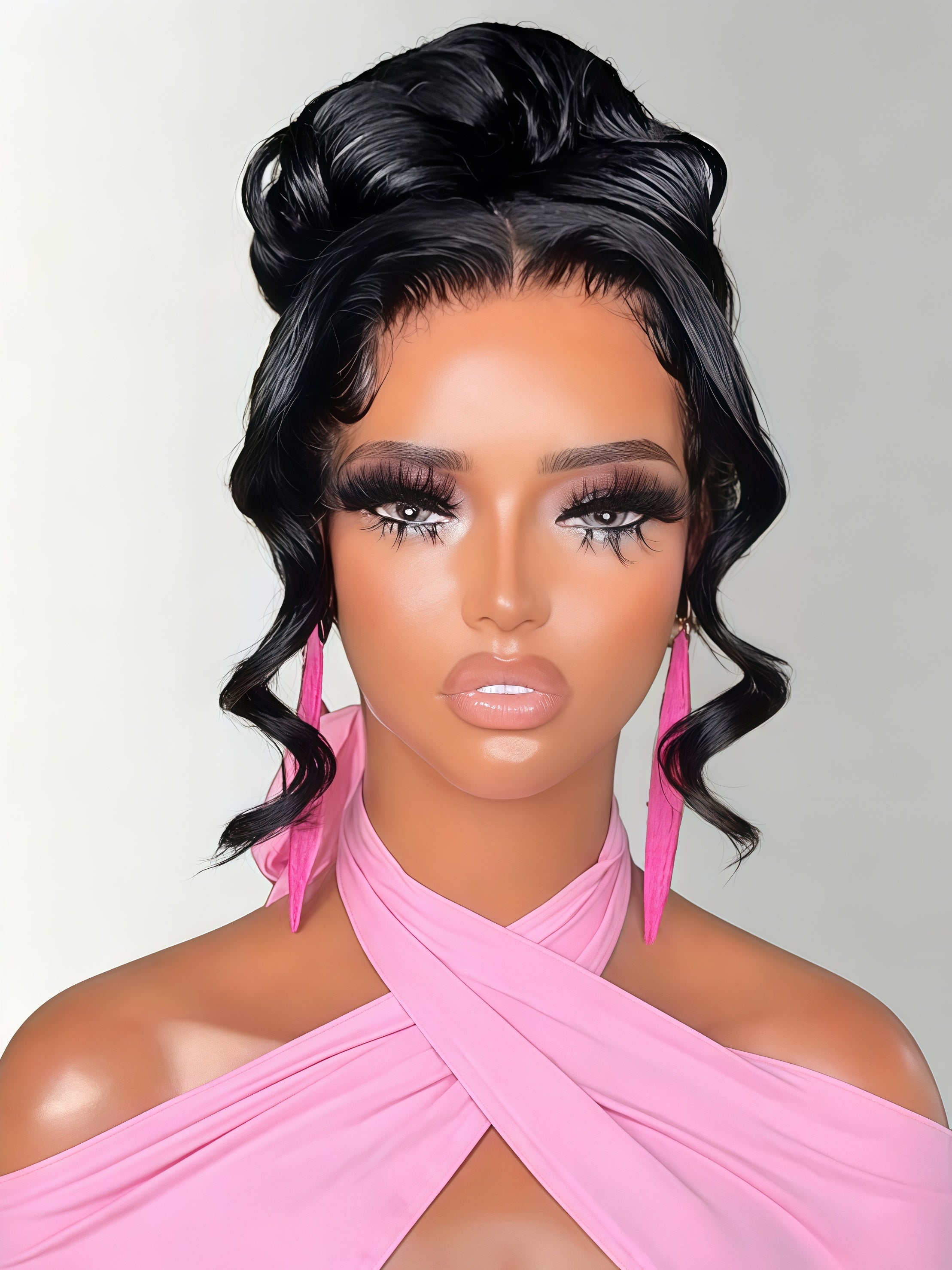 A mannequin bust wearing a voluminous black updo wig with side-swept curls and long pink dangling earrings, styled with a pink draped top against a light gray background.