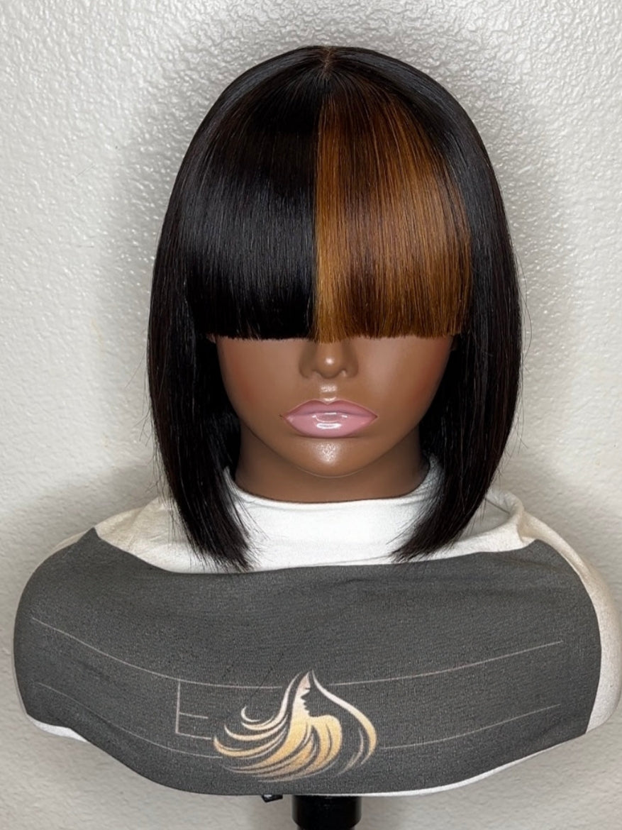 A straight bob wig with a center part, featuring a dark black side and a warm brown center section, displayed on a mannequin head with a gray salon cape.