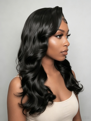 A woman with long, glossy black wavy hair wearing a light beige top, shown in profile against a plain light gray background.
