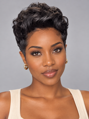 A close-up portrait of a woman with short, curly black hair, wearing gold hoop earrings and a cream ribbed tank top against a solid gray background.