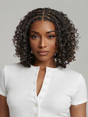 A woman with a short, curly black wig with a center part and braided details at the crown, wearing a white ribbed short-sleeve henley top against a light gray background.
