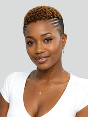 A woman with a short, textured crop hairstyle wearing a white V-neck top and gold necklaces, shown against a solid light gray background.