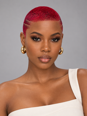 A close-up portrait of a model with a vibrant, short magenta-pink undercut hairstyle and gold hoop earrings, wearing a white one-shoulder top against a solid gray background.