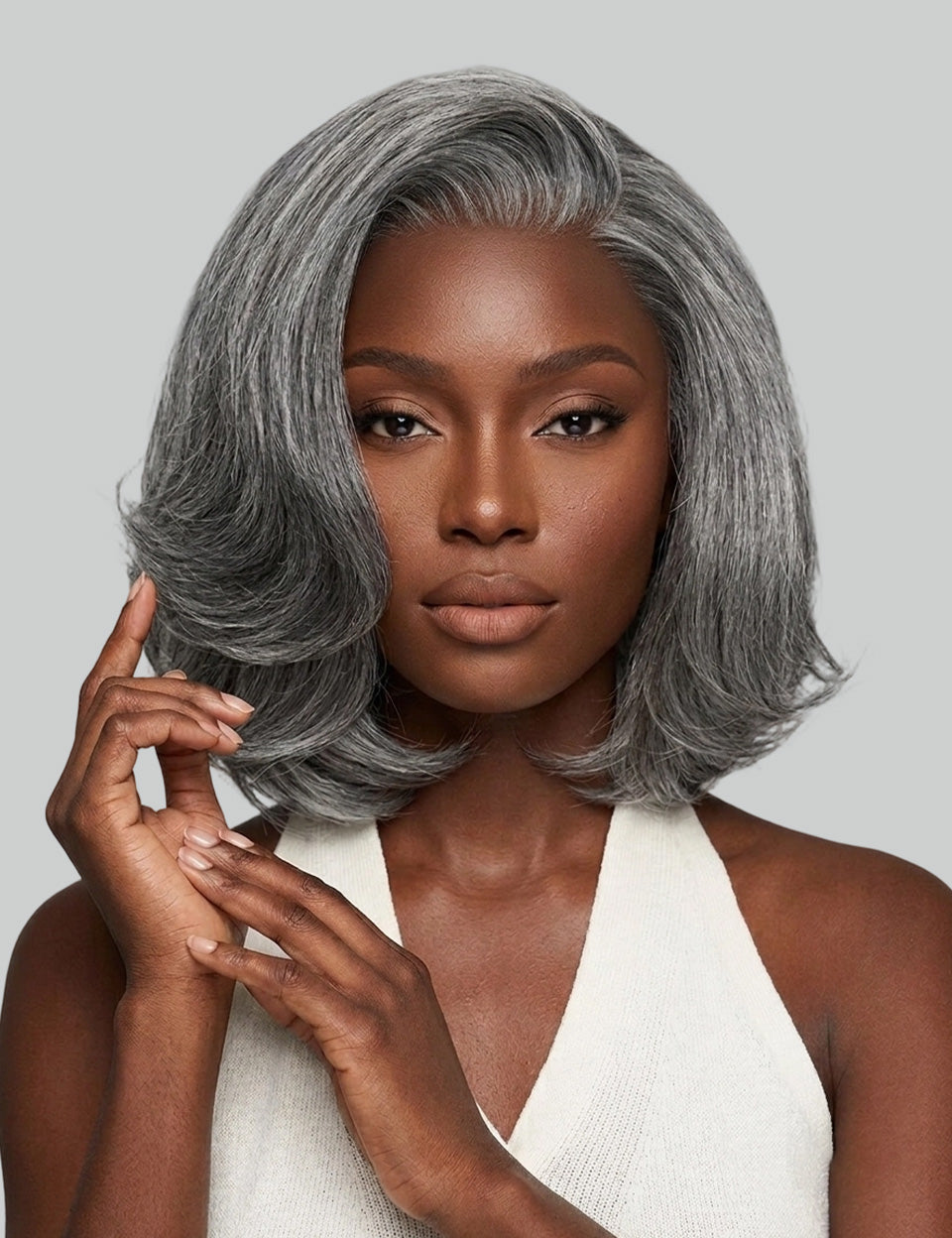 A woman modeling a short, layered gray wig with soft waves and a side-swept bang against a solid light gray background.