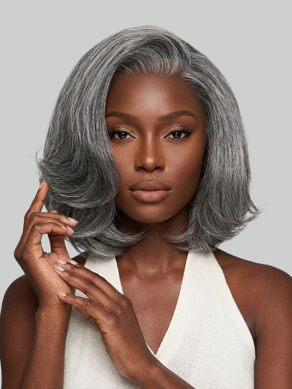 A woman modeling a short, layered gray wig with soft waves and a side-swept bang against a solid light gray background.