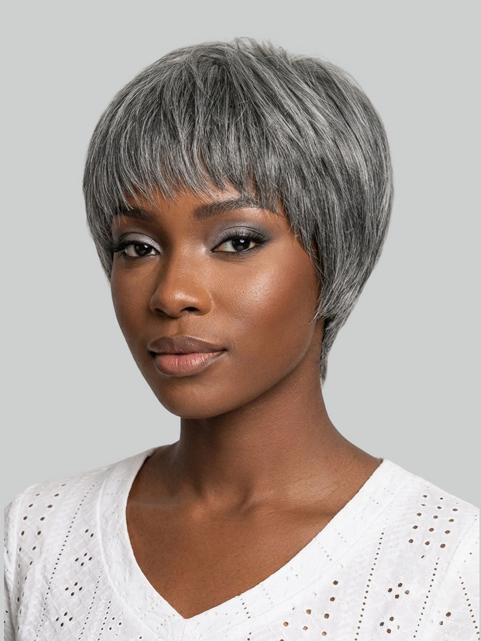 A woman wearing a short, layered gray wig with side-swept bangs, shown against a plain light gray background.