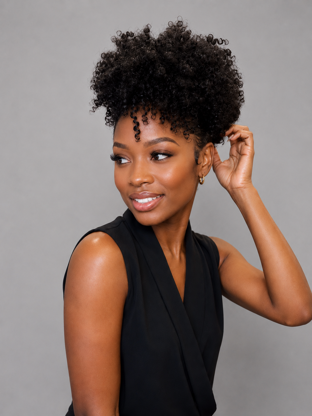 A woman with a voluminous, curly black afro hairstyle wearing a black sleeveless top, posing against a solid gray background.
