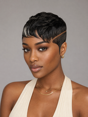 A woman with a short, textured black pixie cut and a side part, wearing a cream halter top and gold jewelry, photographed against a solid gray background.
