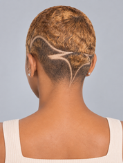 Back view of a person with a short textured haircut featuring a light beige geometric line design shaved into the side of the head, wearing a cream ribbed tank top against a solid light gray background.