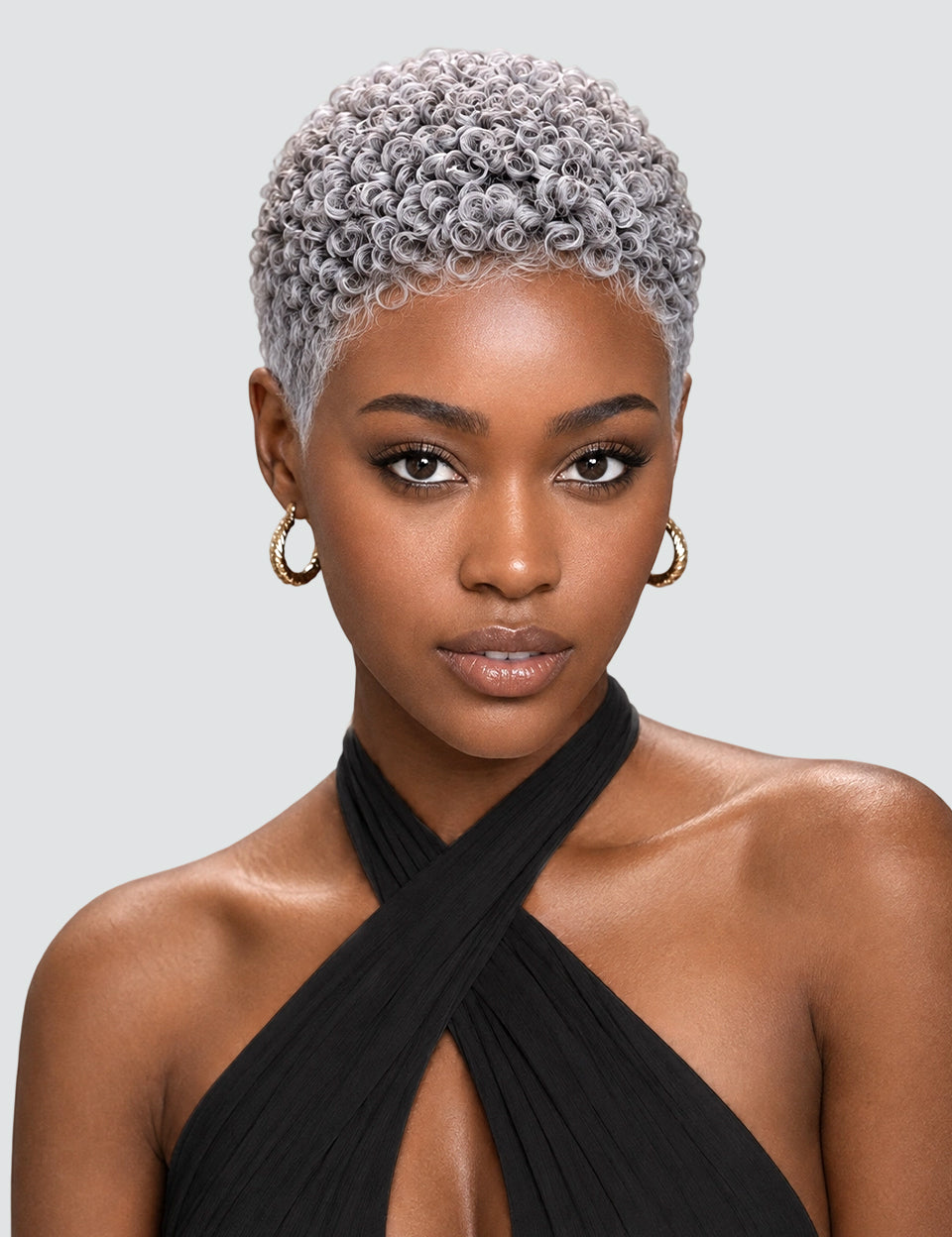 A close-up portrait of a model with a short, tightly curled platinum-blonde wig, wearing gold hoop earrings and a black halter top against a light gray background.