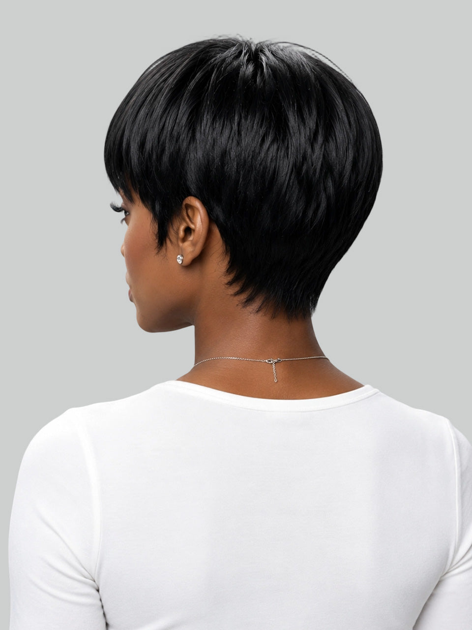 A woman with a high-volume, curly black hair extension or wig styled in a messy bun, wearing a light beige t-shirt against a solid gray background.