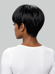 A woman with a high-volume, curly black hair extension or wig styled in a messy bun, wearing a light beige t-shirt against a solid gray background.