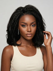 Frontal portrait of a model gently touching her black curly bob wig, revealing the fullness around the face and the natural parting at the crown. Her confident gaze and delicate jewelry accentuate the polished, everyday-ready look. The wig’s texture and volume create a striking contrast against her dark skin tone and light-colored top.