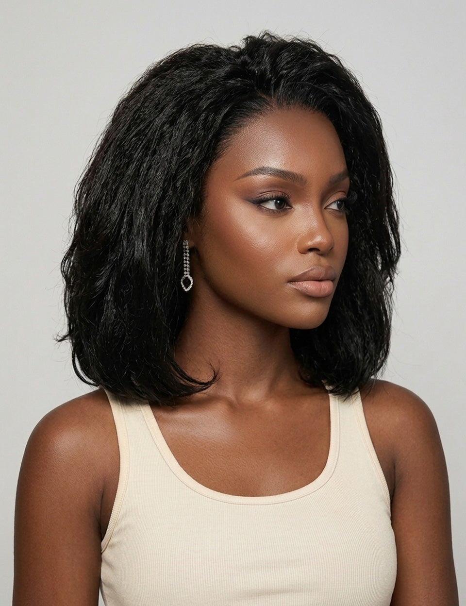 Three-quarter side profile of a woman in a black wavy bob wig, highlighting the gentle curl pattern and smooth transition from crown to ends. Her subtle makeup and dangling crystal earrings complement the sophisticated vibe. The image captures the realistic movement and shine of the hair against a neutral background.