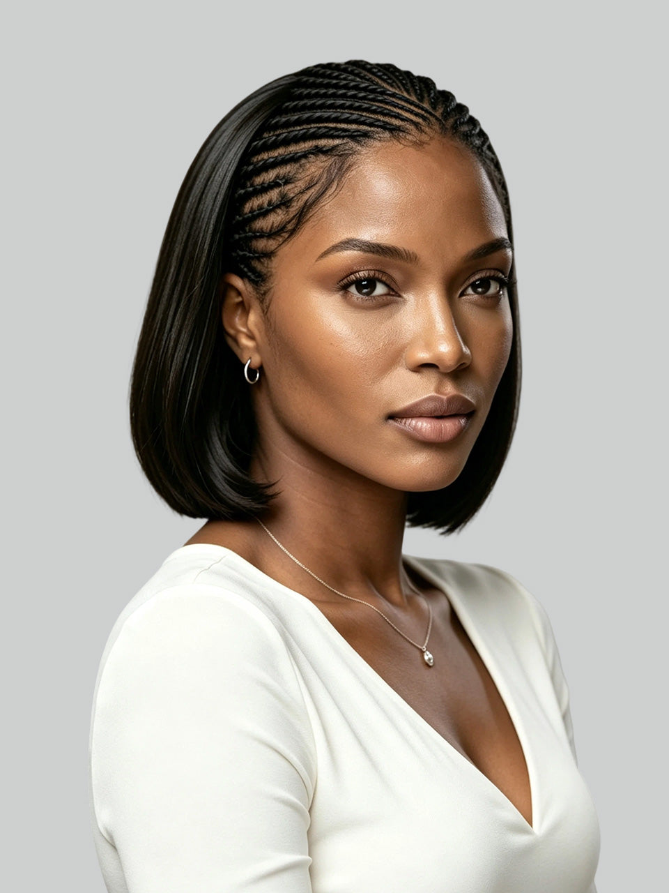 A woman with a sleek, shoulder-length black bob hairstyle featuring detailed cornrow braids across the top and sides, wearing a white V-neck top against a solid gray background.