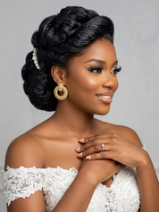 A woman with an elegant updo hairstyle wearing a white lace off-the-shoulder dress, gold hoop earrings, and a ring, posing against a neutral gray background.