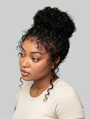 A woman with a high-volume, curly black hair extension or wig styled in a messy bun, wearing a light beige t-shirt against a solid gray background.