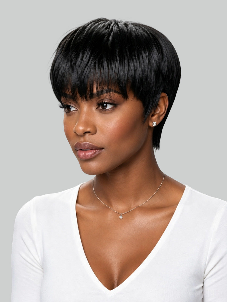 A woman with a short, straight black wig with side-swept bangs, wearing a white V-neck top and a delicate necklace, shown against a solid gray background.