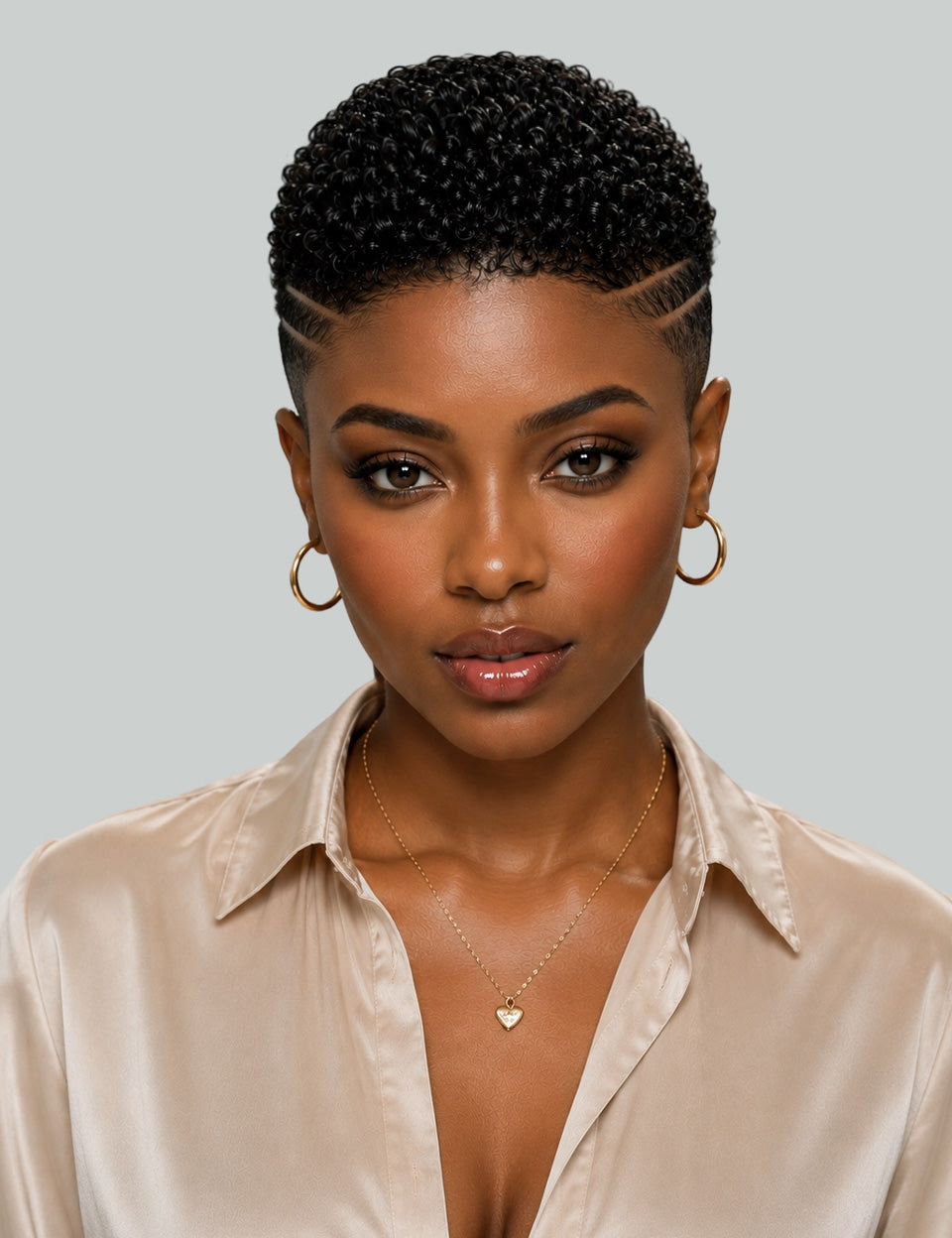 A close-up portrait of a woman with a short, tightly curled black wig, styled with a side part and gold hoop earrings, wearing a champagne satin shirt against a solid gray background.