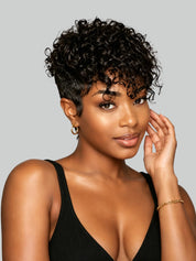 A woman with short, curly black hair and a side-swept undercut hairstyle, wearing a black ribbed tank top against a solid gray background.