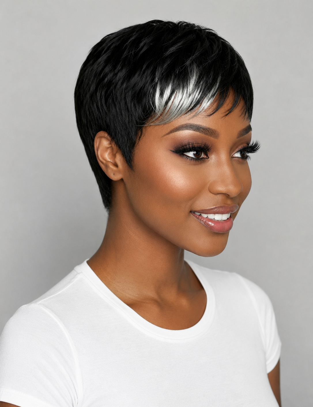 A woman wearing a short black pixie wig with a bold silver streak through her hair, styled with a white crew-neck t-shirt against a neutral gray background.