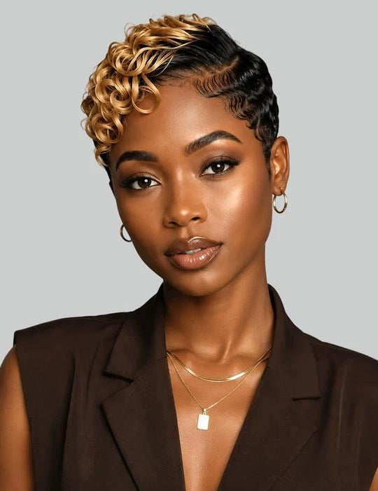 A woman with a short, styled curly wig in black and blonde highlights, wearing a dark brown sleeveless blazer and gold jewelry against a solid gray background.
