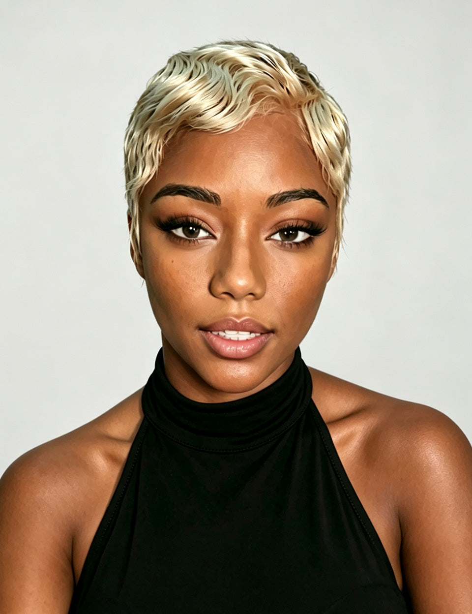 A close-up portrait of a woman with a short, textured platinum blonde wig, wearing a black halter top against a light gray background.