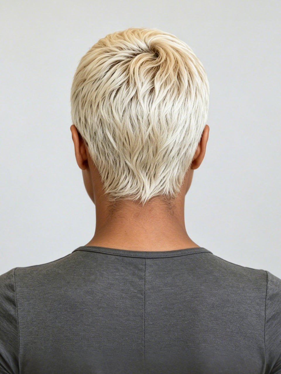 Back view of a person with a short, layered, textured blonde hairstyle wearing a dark gray t-shirt against a light gray background.