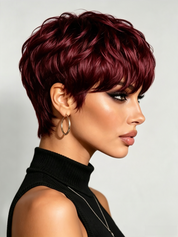 A woman in profile wearing a short, layered, textured wig in deep burgundy red. The wig is styled with a side-swept bang and is shown against a plain light gray background.