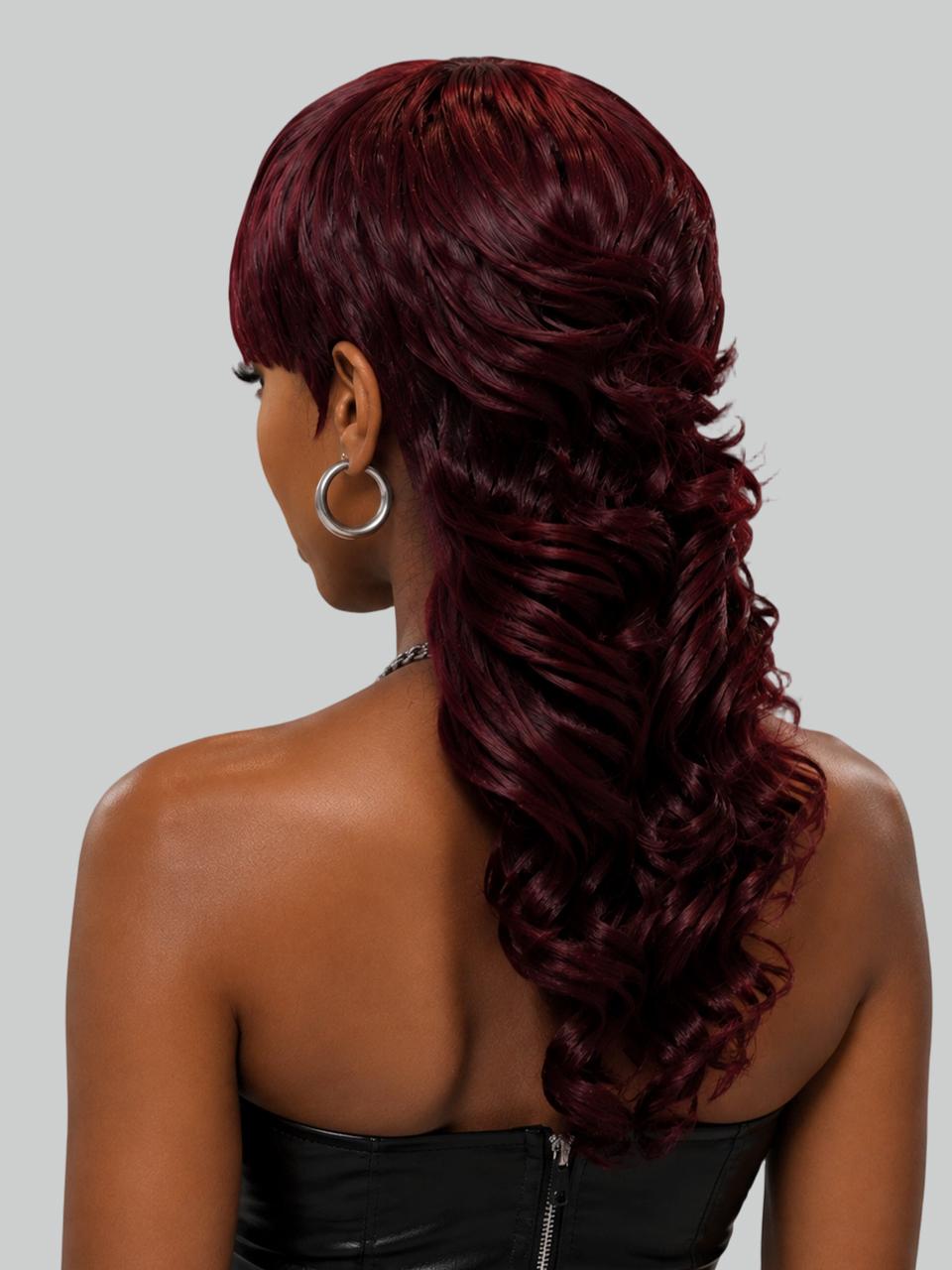 A woman in profile with a short, curly red hairstyle and shaved side details, wearing gold hoop earrings and a cream halter top against a light gray background.