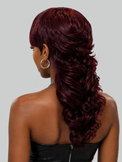 A woman in profile with a short, curly red hairstyle and shaved side details, wearing gold hoop earrings and a cream halter top against a light gray background.