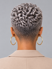 Back view of a person with a short, textured, salt-and-pepper curly wig or hairpiece, wearing large gold hoop earrings and a beige blazer against a solid gray background.