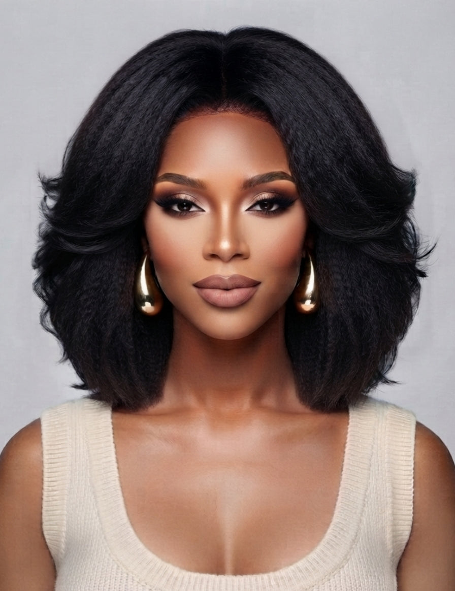 Frontal portrait of a woman in a black center-parted wave wig, emphasizing the realistic lace front hairline and symmetrical curl pattern. The full-bodied style and polished finish make it ideal for both casual and formal occasions, enhanced by minimalist gold hoop earrings.