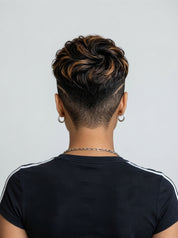 Back view of a person with a styled high-top fade haircut, wearing a black t-shirt with white shoulder stripes and small hoop earrings, against a light gray background.